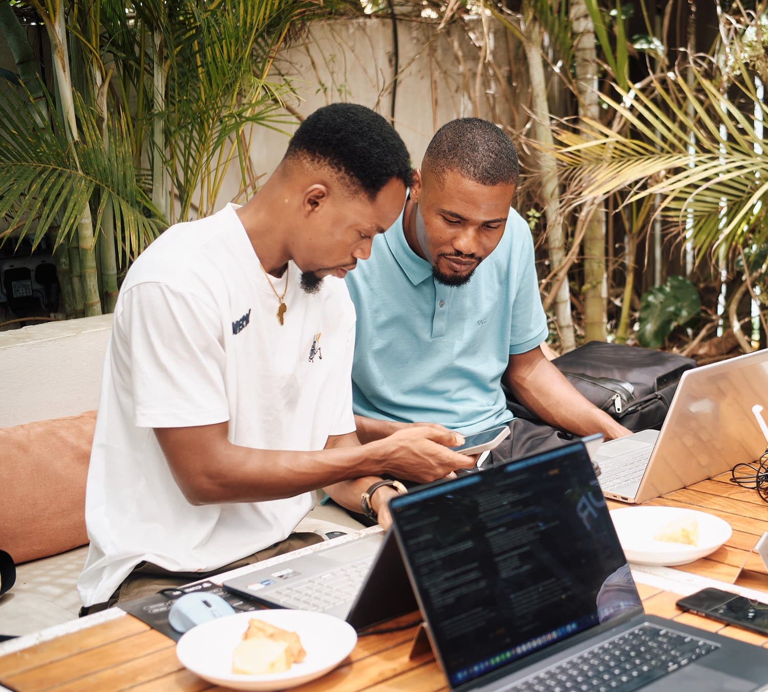 Clemence working through something on his phone with a friend, laptops open at an outdoor café table